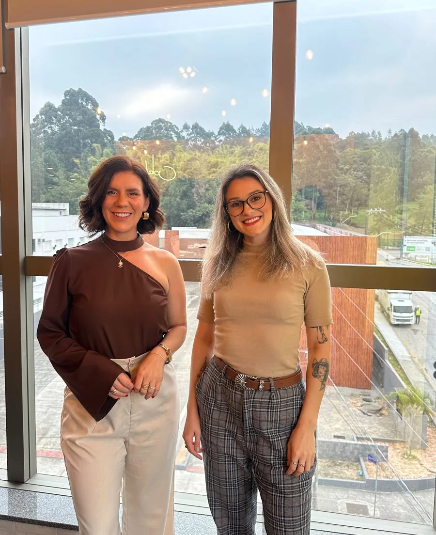 Michelle Moratelli e Izabel Zanotto em pé diante de uma janela de escritório